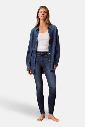 Jean skinny en denim bleu moyen de Calvin Klein, avec un tanktop blanc et une chemise en denim.