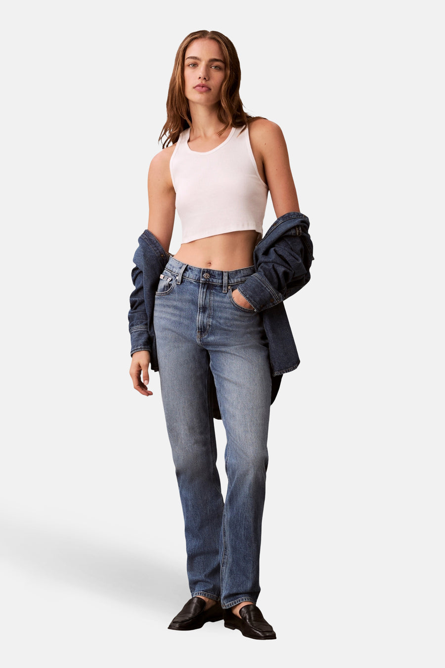 Mid blue mom jeans van Calvin Klein, met een denim jas losjes over de schouders en een wit topje.

