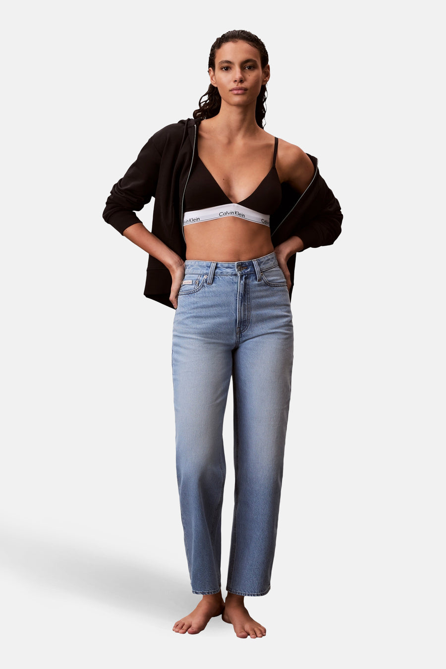 Jean coupe spéciale en denim bleu clair de Calvin Klein, avec une taille haute et des jambes droites, stylisé avec un sweat à capuche noir et un soutien-gorge noir.