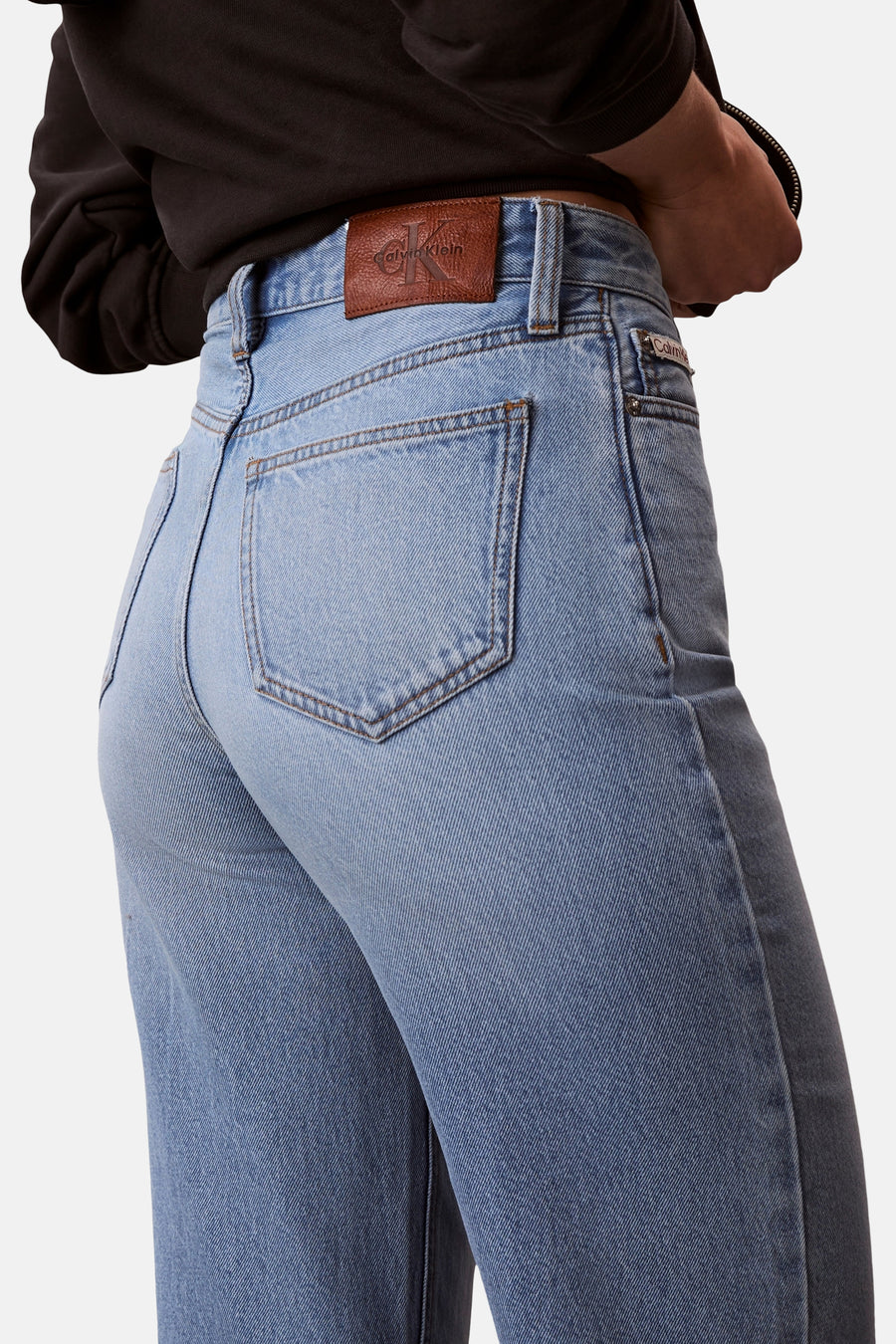 Jean coupe spéciale en denim bleu clair de Calvin Klein, avec poche arrière et étiquette de marque en cuir marron sur la ceinture.