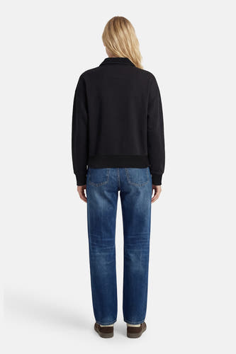 Pull noir de Calvin Klein, à longues manches, porté avec des jeans et des chaussures marrons, vu de dos.