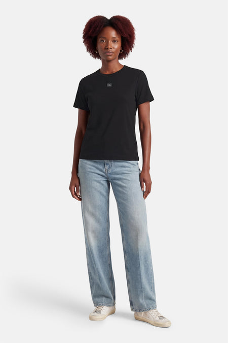 T-shirt noir Calvin Klein, avec un petit logo sur la poitrine, combiné avec un jean bleu et des baskets blanches.