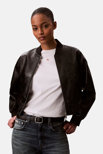 T-shirt blanc Calvin Klein, porté sous un blouson bomber en cuir noir avec une fermeture éclair argentée.