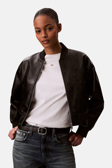 T-shirt blanc Calvin Klein, porté sous un blouson bomber en cuir noir avec une fermeture éclair argentée.