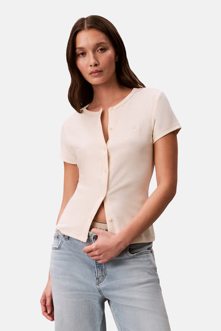 Gilet écru de Calvin Klein, porté avec un cardigan beige et un jean ample avec un long trench-coat.