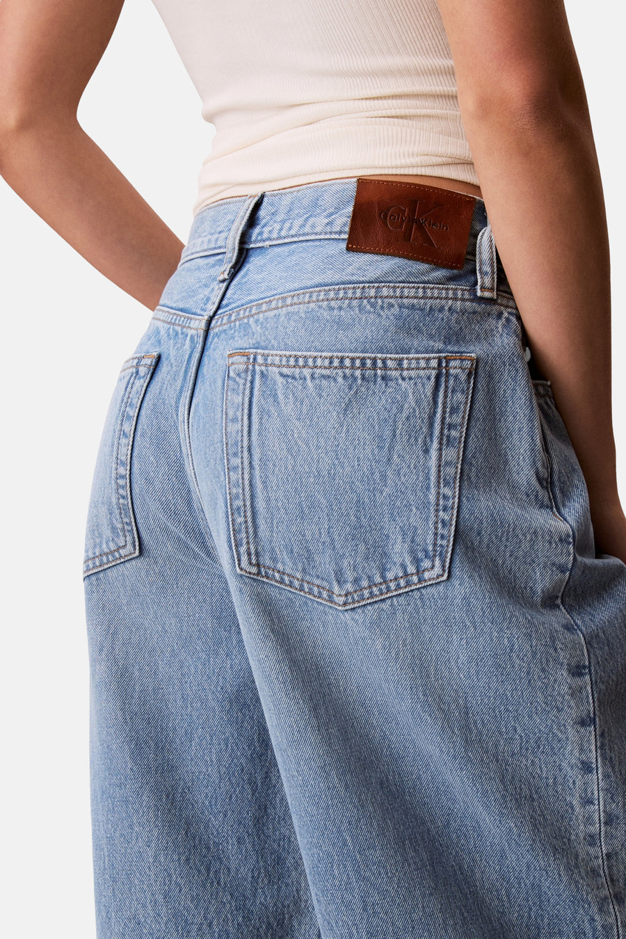 Jean en denim bleu clair Calvin Klein avec écusson logo en cuir marron, poches arrière et un haut légèrement côtelé.