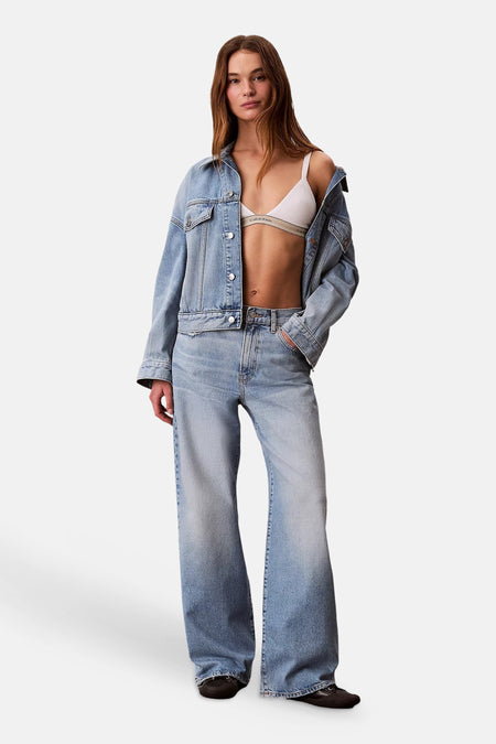 Jean large bleu clair en denim de Calvin Klein, porté par un mannequin avec une veste en jean et une bralette blanche.