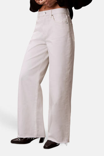 Jean blanc coupe large en denim écru de Calvin Klein, avec écusson logo en cuir marron et poches plaquées au dos.