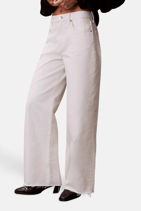 Jean blanc coupe large en denim écru de Calvin Klein, avec écusson logo en cuir marron et poches plaquées au dos.