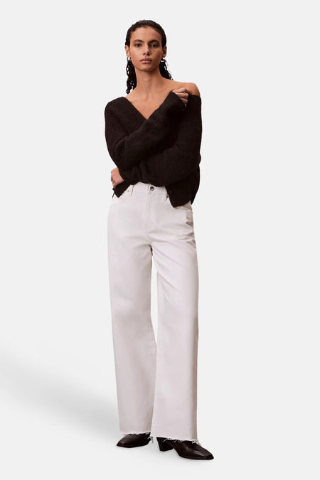 Jean large blanc cassé en denim Calvin Klein à ourlets effilochés, porté par un mannequin avec un pull noir et des bottines.