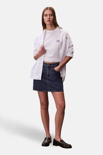 T-shirt blanc à manches courtes Calvin Klein, avec une chemise blanche ample et une jupe en jean bleu foncé.