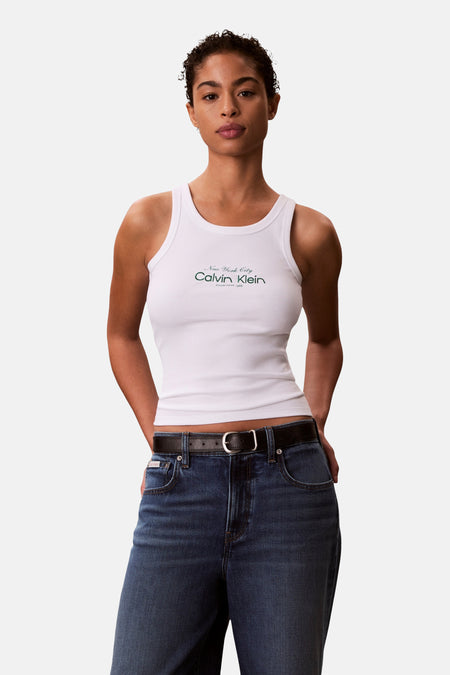 Débardeur blanc Calvin Klein, avec impression de logo, combiné avec un jean bleu foncé et une ceinture en cuir noir.