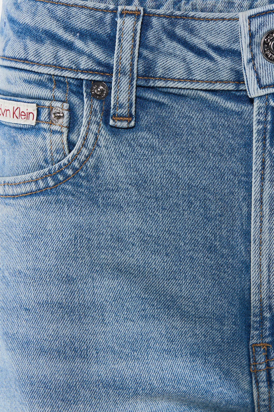 Lichtblauwe skinny bootcut jeans van Calvin Klein, met verbleekt denim, bruine naden en zilveren knopen, close-up vooraanzicht