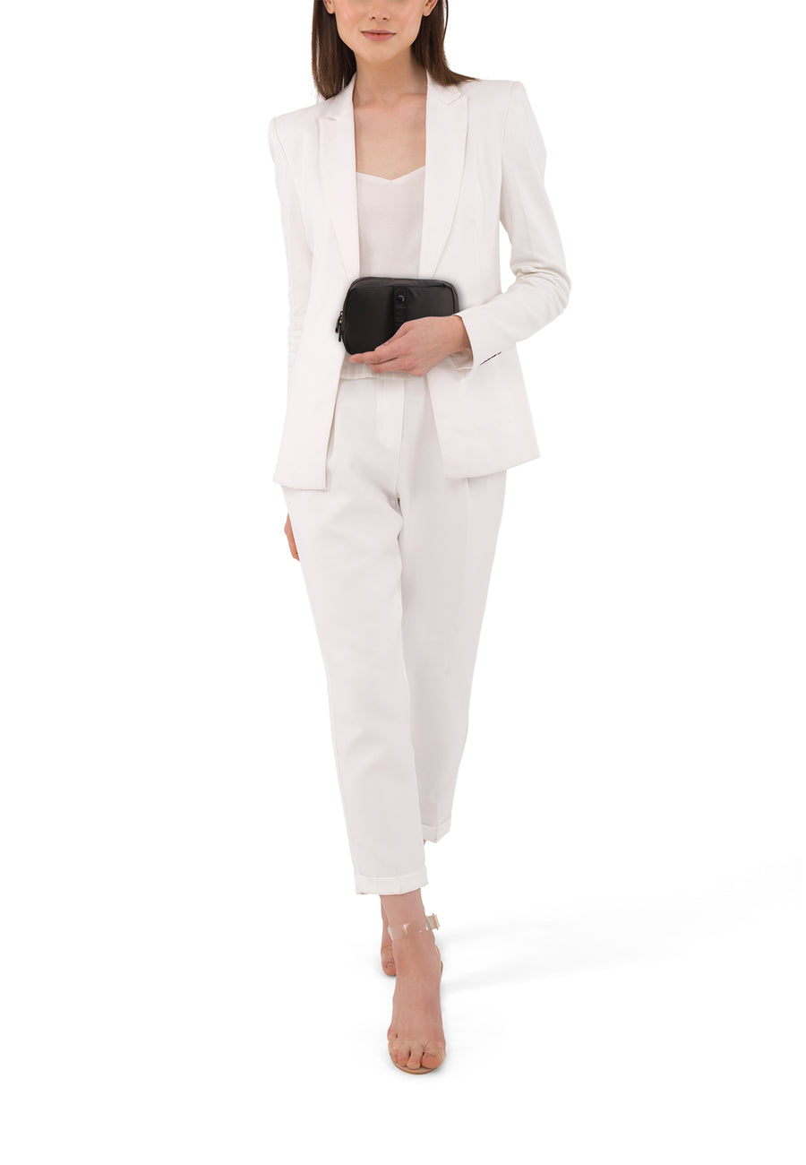 Vrouw in witte broekpak met zwarte tas en transparante hakken.