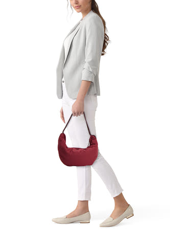Sac à bandoulière bordeaux de Calvin Klein, porté par une femme avec un blazer gris, un pantalon blanc et des mocassins beiges.
