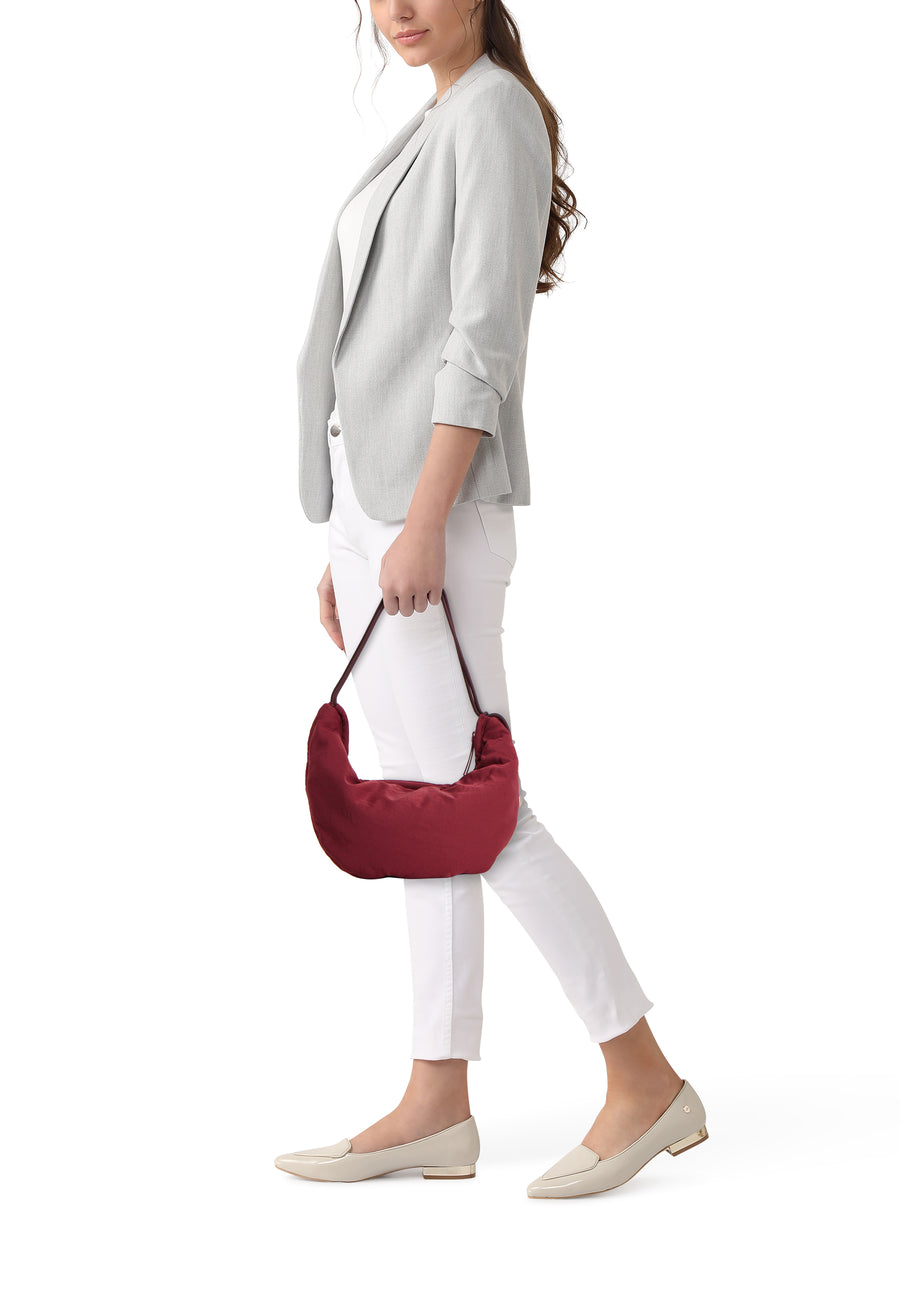 Sac à bandoulière bordeaux de Calvin Klein, porté par une femme avec un blazer gris, un pantalon blanc et des mocassins beiges.
