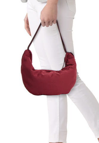 Sac à bandoulière bordeaux de Calvin Klein, porté par un mannequin en pantalon blanc et pull gris.