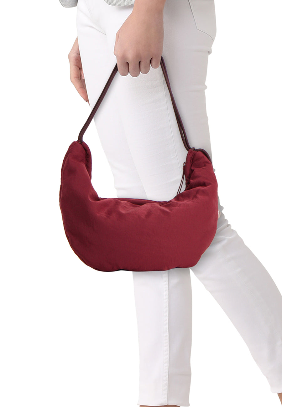 Sac à bandoulière bordeaux de Calvin Klein, porté par un mannequin en pantalon blanc et pull gris.