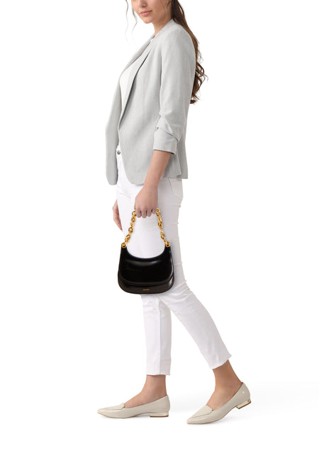 Vrouw draagt grijze blazer, witte broek en beige loafers, met een zwarte Calvin Klein handtas met gouden ketting.