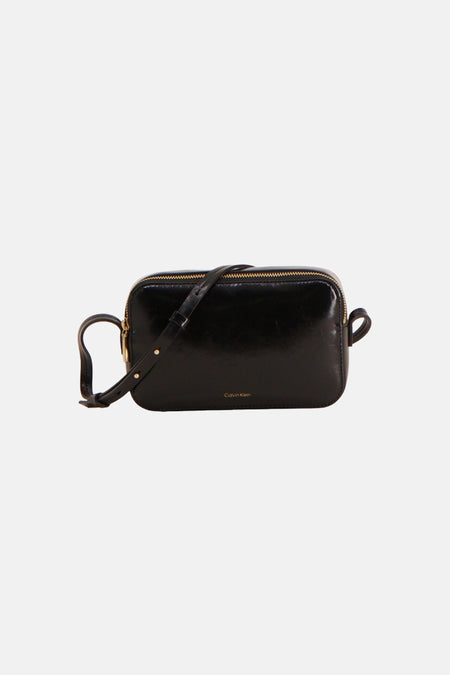 Sac à bandoulière rectangulaire noir de Calvin Klein, en matière brillante aspect cuir légèrement grainé avec des passants sur les côtés.