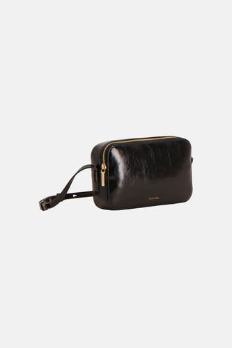 Sac à bandoulière noir brillant Calvin Klein avec fermeture éclair dorée, bandoulière réglable et petit logo, présenté en biais.