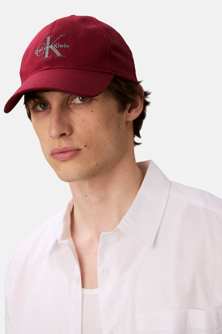 Casquette rouge de Calvin Klein, avec logo brodé sur l'avant, portée par un modèle en chemise blanche.