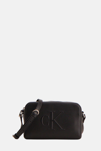 Sac à dos noir Calvin Klein avec un logo CK en relief et une sangle d'épaule ajustable, porté sur un t-shirt blanc et des jeans.