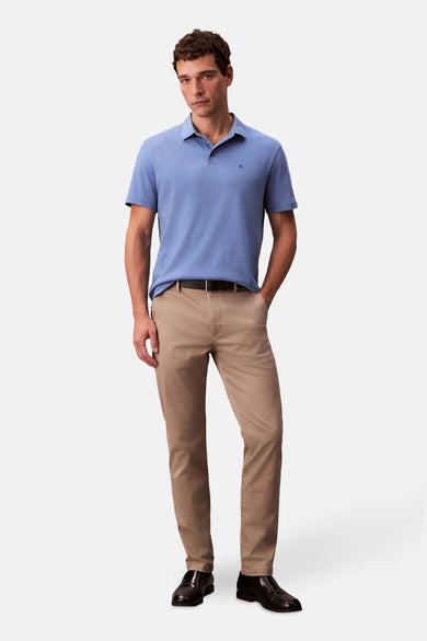 Polo bleu avec manches courtes de Calvin Klein, associé à un pantalon khaki et une ceinture en cuir.