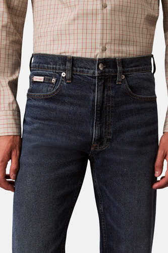 Jean bleu marine droit de Calvin Klein, avec des coutures subtiles et une chemise à carreaux beige.