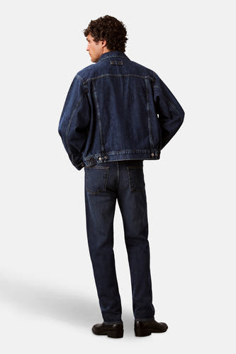 Jean bleu marine droit de Calvin Klein, vu de derrière, avec une veste en denim coordonnée et des chaussures noires.