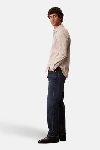 Jean bleu marine droit de Calvin Klein, porté par un homme en un chemisier à carreaux et des chaussures noires.