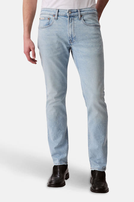 Jean slim fit en denim bleu clair de Calvin Klein, avec un style cinq poches traditionnel et des chaussures noires.