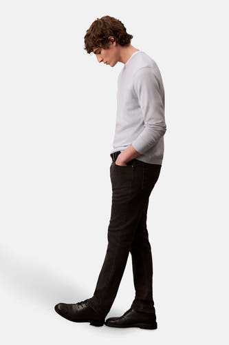 Jean slim fit denim noir de Calvin Klein, modèle debout en vue latérale avec les mains dans les poches.