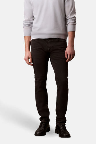 Jean slim noir Calvin Klein, porté avec une chemise grise claire et des chaussures en cuir noires.