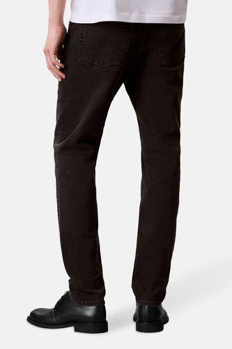 Jean tapered de denim gris foncé de Calvin Klein, vu de de derrière avec des chaussures en cuir noir et un T-shirt blanc.