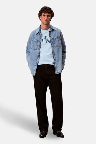T-shirt bleu à manches courtes de Calvin Klein, avec un grand logo CK, associé à une chemise en denim et à un pantalon noir.