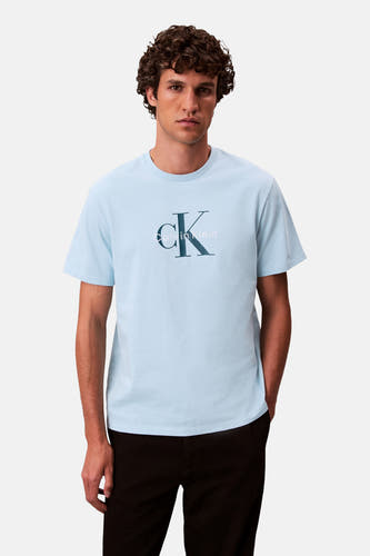 T-shirt bleu à manches courtes de Calvin Klein, avec logo sur la poitrine et porté avec un pantalon noir.