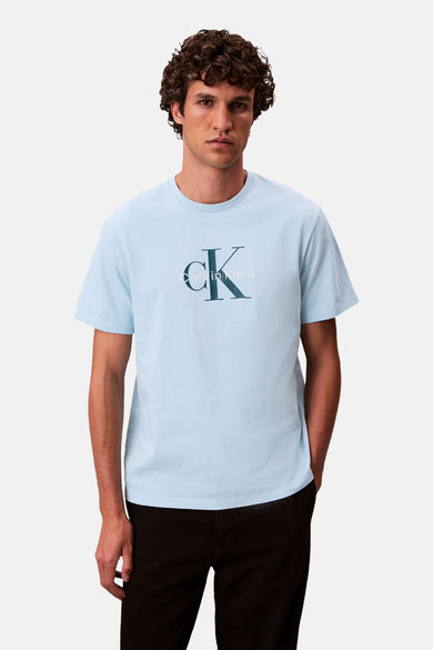 T-shirt bleu à manches courtes de Calvin Klein, avec logo sur la poitrine et porté avec un pantalon noir.