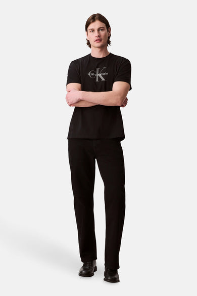T-shirt noir à manches courtes de Calvin Klein, porté avec des jeans noirs et des chaussures, les bras croisés.