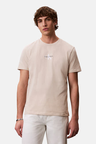 T-shirt écru à manches courtes de Calvin Klein, porté avec un pantalon blanc et un bracelet argenté.