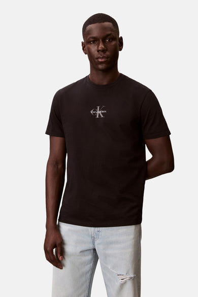 T-shirt noir à manches courtes Calvin Klein avec logo CK argenté sur la poitrine, porté par un mannequin avec un jean bleu clair déchiré.