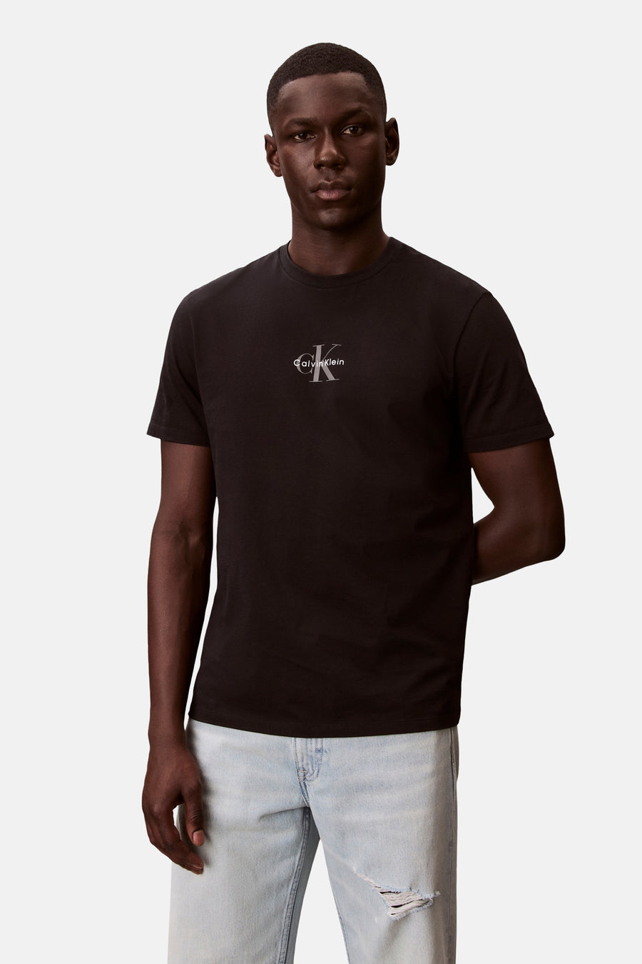 T-shirt noir à manches courtes Calvin Klein avec logo CK argenté sur la poitrine, porté par un mannequin avec un jean bleu clair déchiré.