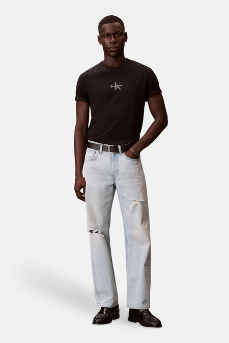 T-shirt noir à manches courtes de Calvin Klein, avec logo discret et manches retroussées, porté par un homme avec un jean légèrement délavé.