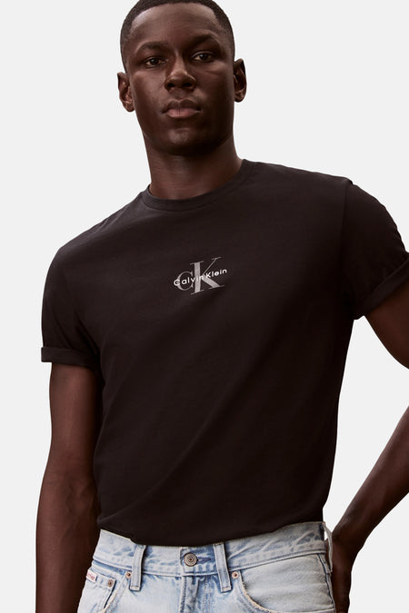 T-shirt noir à manches courtes de Calvin Klein, avec logo argenté sur la poitrine et manches retroussées, porté par un homme avec un jean clair.