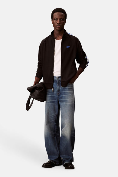 Gilet noir Calvin Klein, avec des rayures blanches sur les manches et un T-shirt blanc en dessous.