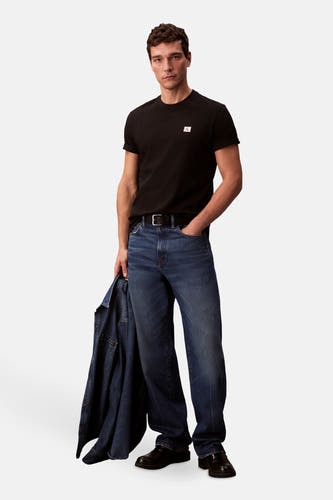 T-shirt noir à manches courtes de Calvin Klein, avec logo sur la poitrine, associé à des jeans et des chaussures noires.