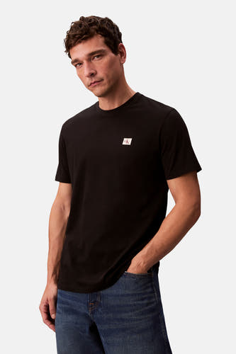 T-shirt noir à manches courtes de Calvin Klein, porté avec un jean bleu et une main dans la poche.