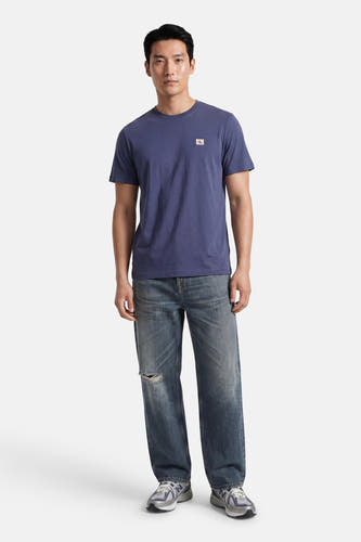 Blauwe korte mouw T-shirt van Calvin Klein met klein logo op borst, gedragen met versleten jeans en sneakers, front view