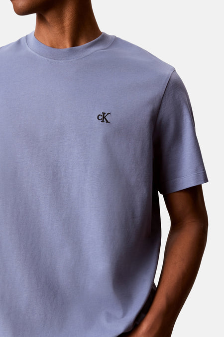 Blauw T-shirt van Calvin Klein met geborduurd cK-logo op de borst, gedragen door een persoon.