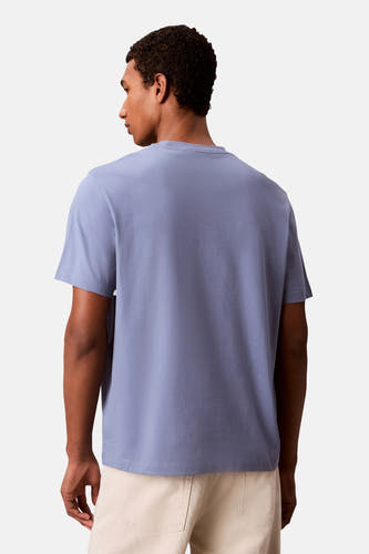 T-shirt à manches courtes bleu clair Calvin Klein, porté par un homme, vue de dos, avec un pantalon beige.